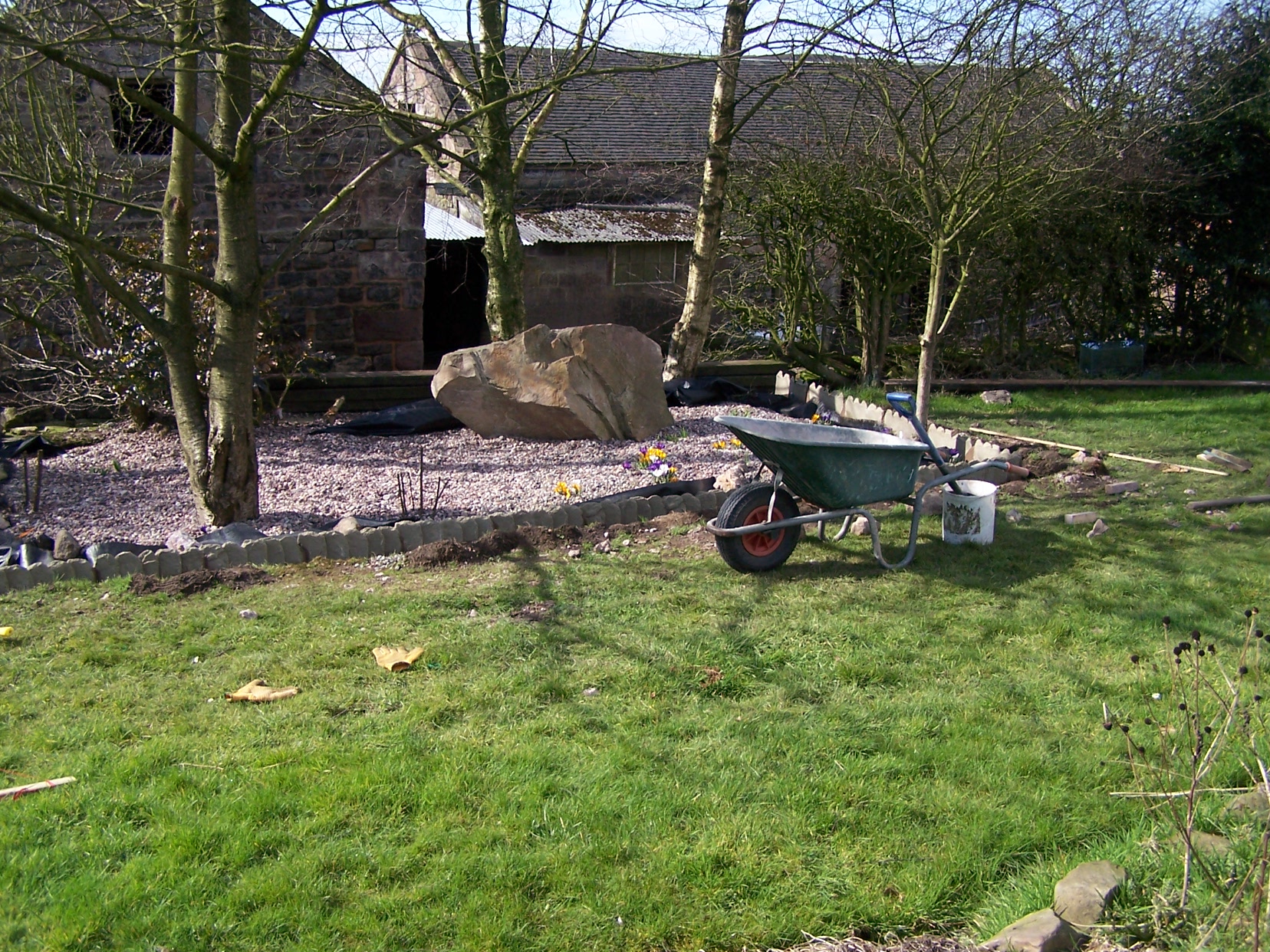 Wheelbarrow in front of gravel garden surrounded by lawn