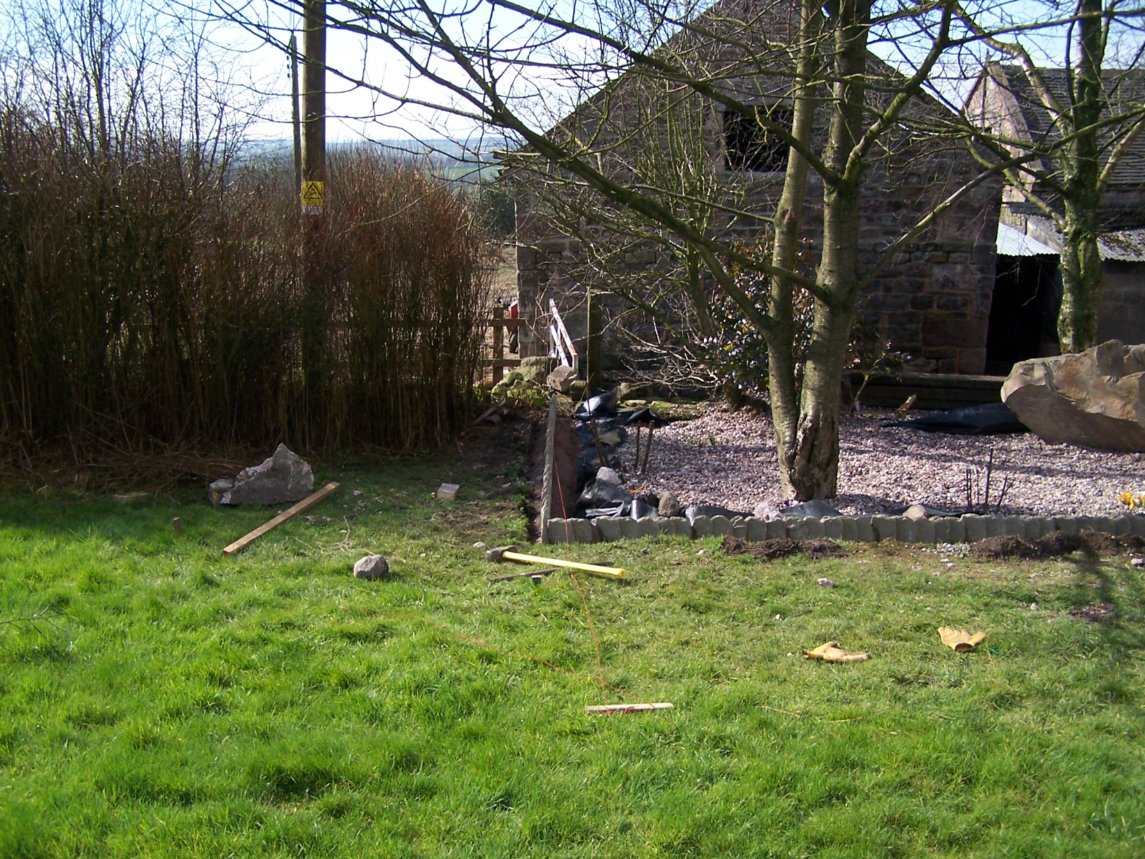 Tools strewn across lawn in front of gravel bad bith tree and boulder