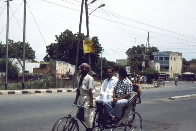 Two men travelling along a main road in Agra by bicycle rickshaw